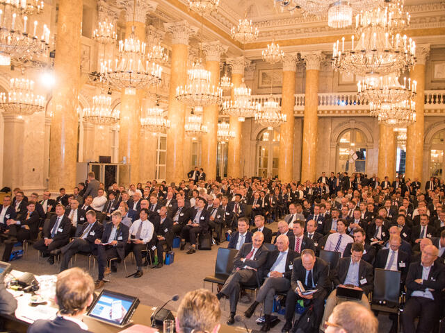 Besucher im Anzug sitzen im Saal mit leuchtenden Kronleuchtern