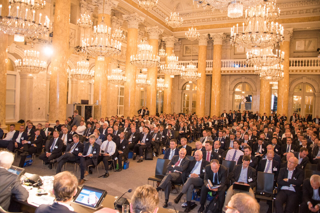 Besucher im Anzug sitzen im Saal mit leuchtenden Kronleuchtern